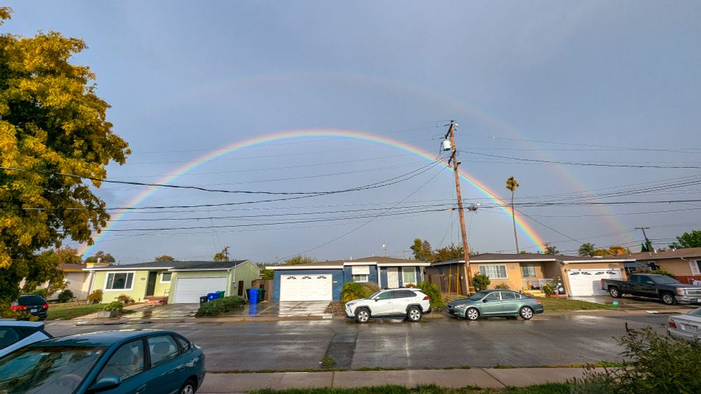 A double rainbow against pretty dark skies, obscured by electrical wires.