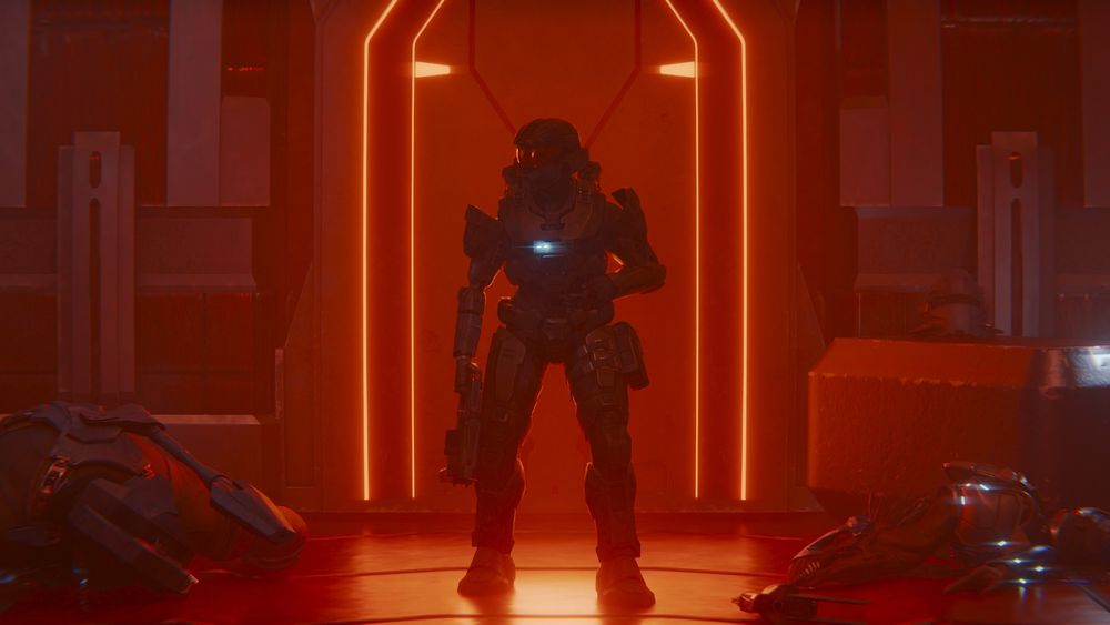 A wounded female SPARTAN-IV standing in front of a doorway on a Banished ship next to a dead brute and jackal. She's holding a Mangler in her right hand and putting pressure on her wound with her left hand.