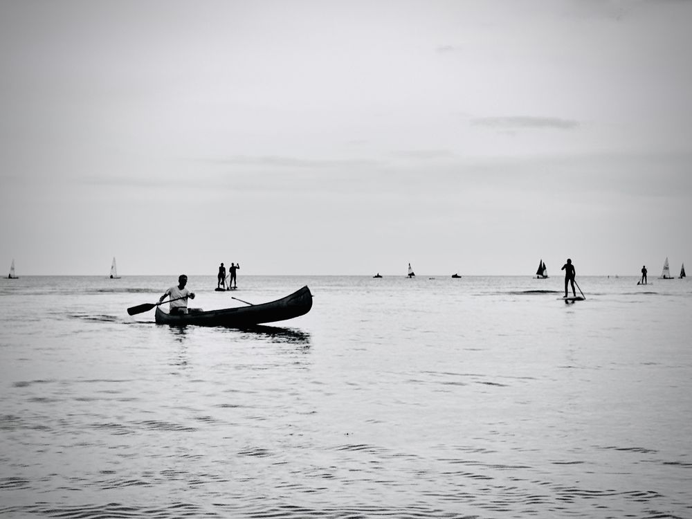 This is a black & white, mono photograph of a summer's day in Newport Bay, Pembrokeshire, Wales with lots of people out enjoying themselves on the water, sailing, paddle boarding and canoeing. The photo was taken on 18 August 2025.