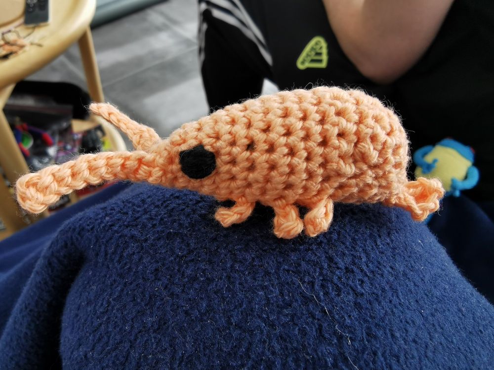 Small crochet doll of a salmon coloured shrimp with big black eyes. 
