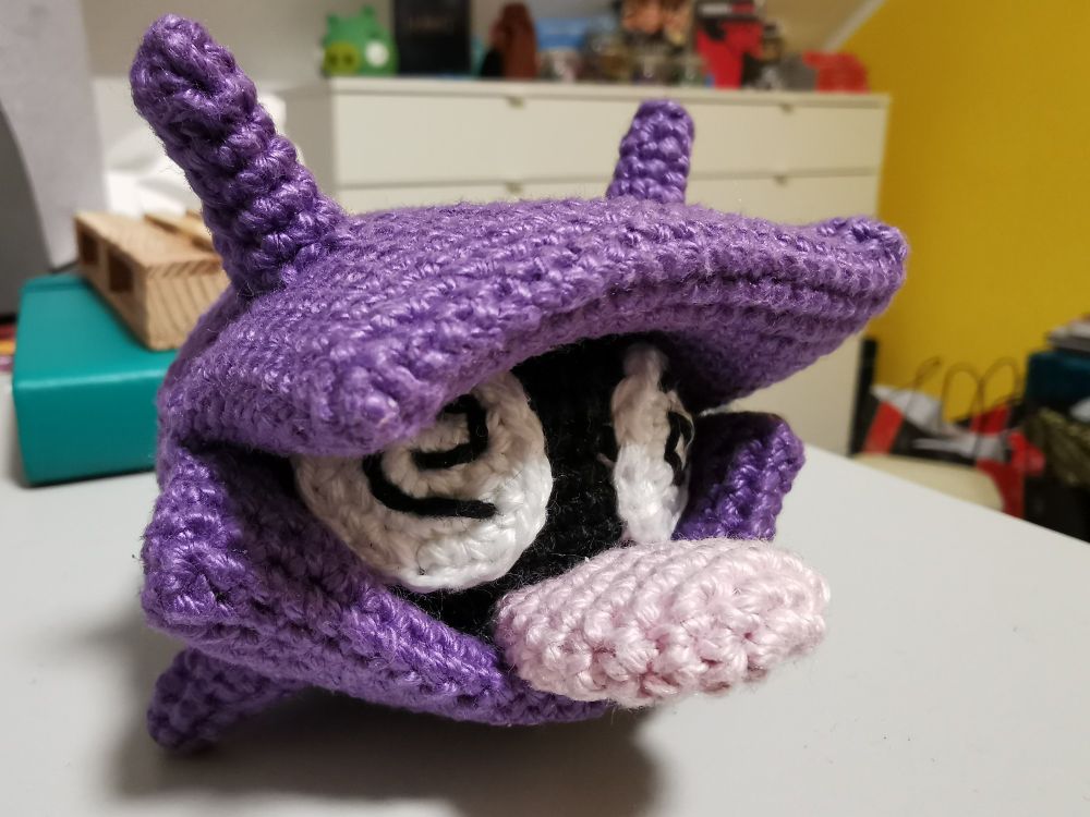 A crocheted Shellder Pokemon with swirly eyes like it's unconscious. 