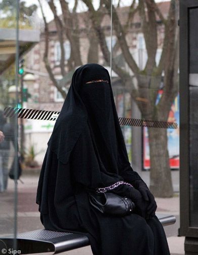 Women sitting on a bench wearing a Face Veil and a Cloak that cover her entire body leaving a slit for her eyes 
