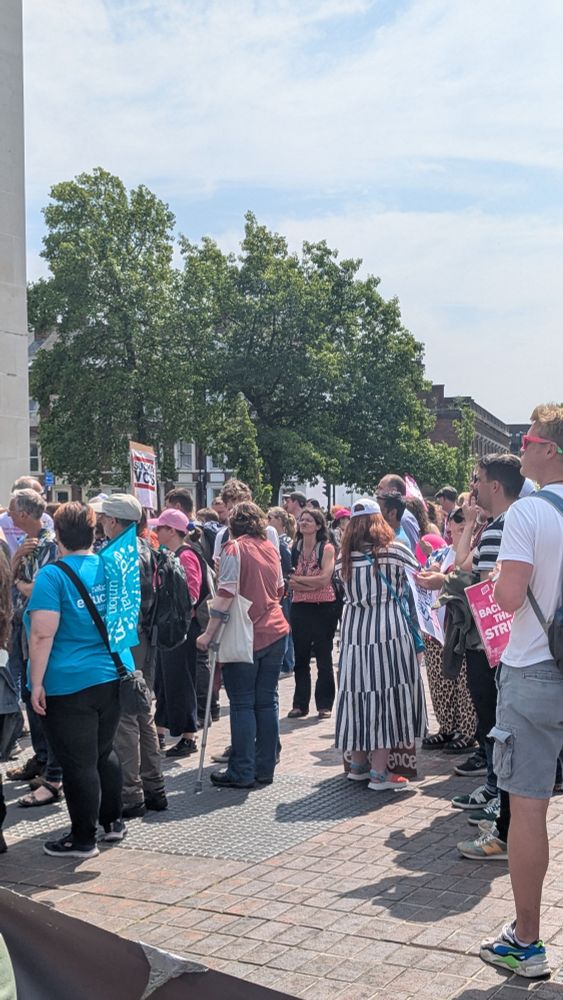 A crowd of people with placards and banners with trees in the background.