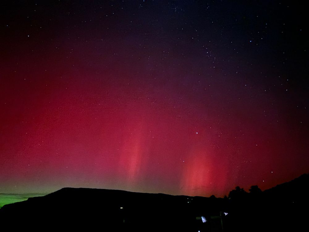 Vertical stripes of red light with green on the horizon above dark mountains.