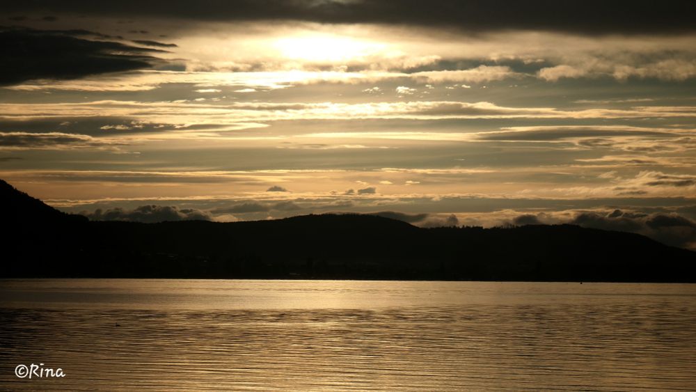 Sunset at Lake Constance, the sky with clouds and the water shine golden.