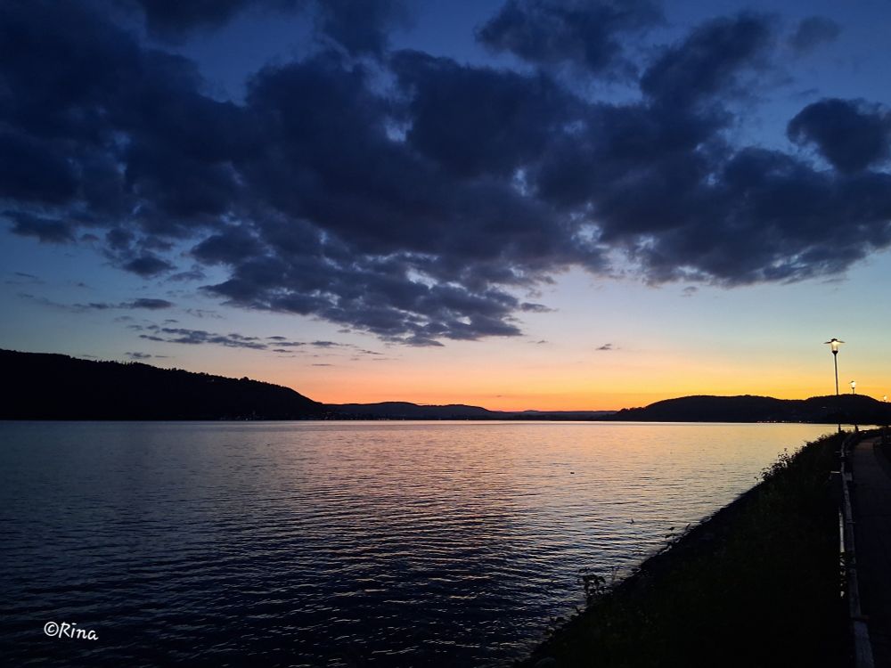 The photo shows the end of the lake. The sun has set and you can see a yellow-red stripe on the horizon.  There are dark clouds in the sky