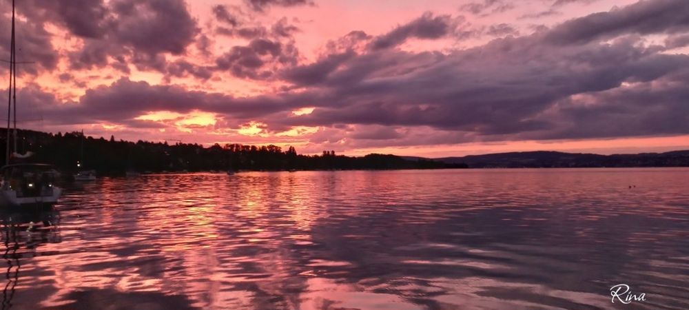 Sunset behind clouds on a lake. The water is pink in color, the clouds grayish blue