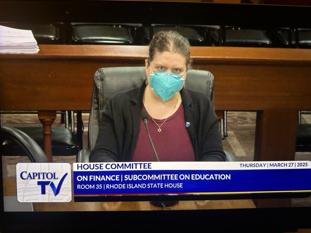 A person in a blazer and face mask sitting at a desk with a chronic reading "Capitol TV House Committee on Finance | Subcommittee on Education Room 35 Rhode Island State House"