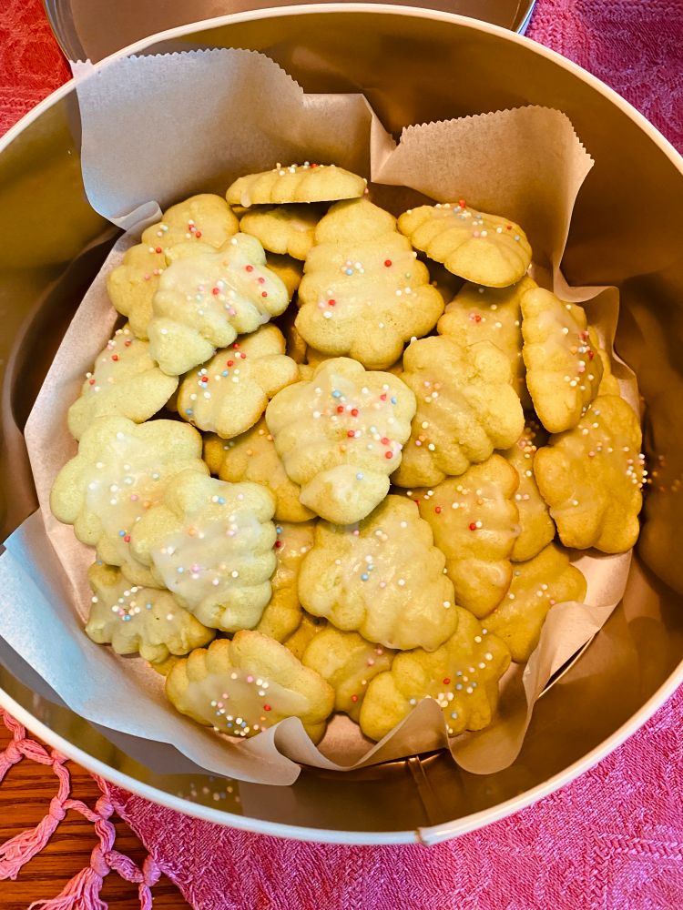 Spritz-kjeks i en boks. De er smørkaker formet som små juletrær, med strø på. 