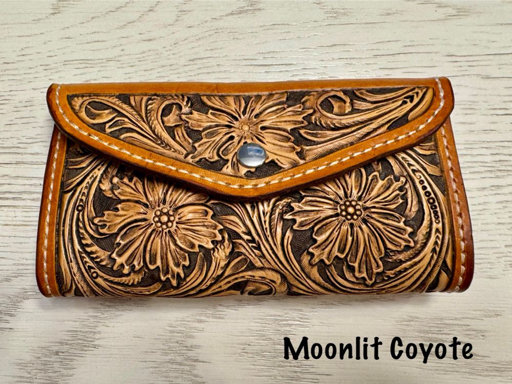 Image of a hand made and tooled leather clutch wallet. The border of the wallet has been dyed a golden brown color while the tooled floral portion has been left the natural leather color. The wallet has been sewn together using ivory thread. 