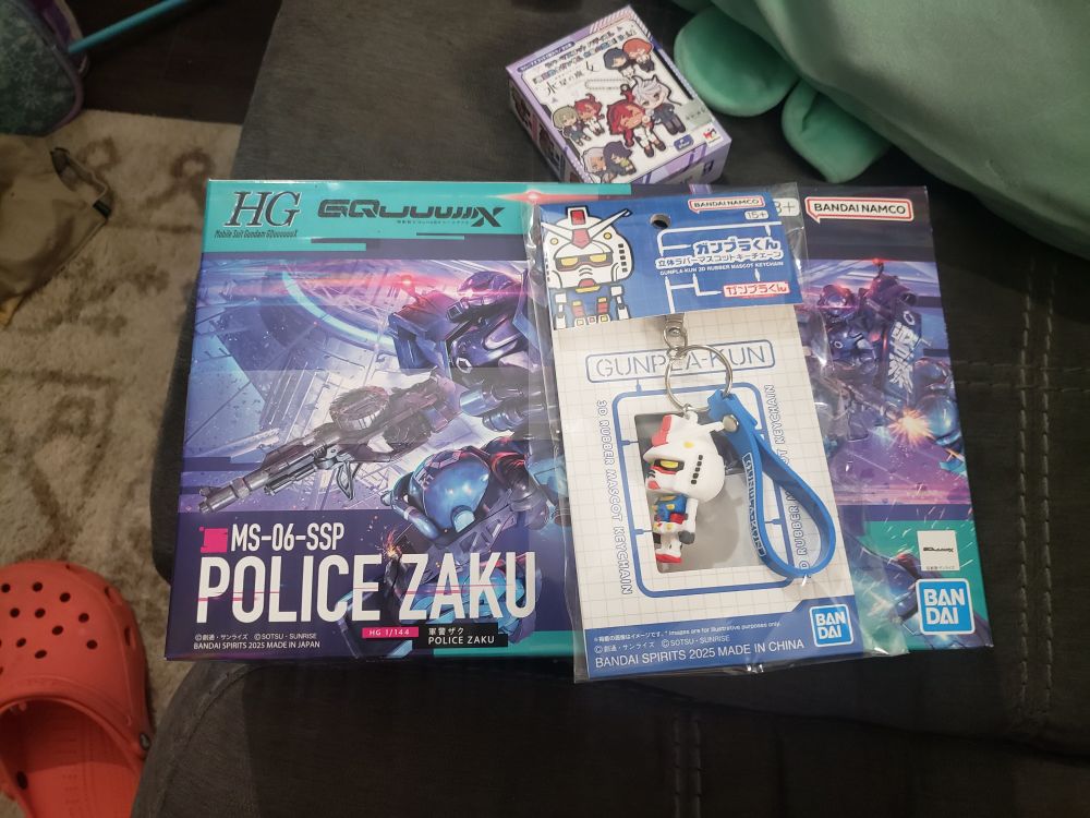 Model robot kit box with Police Zaku from the GQuuuuuux Gundam show.  
Atop the box is a Gundam key chain and a blind box.