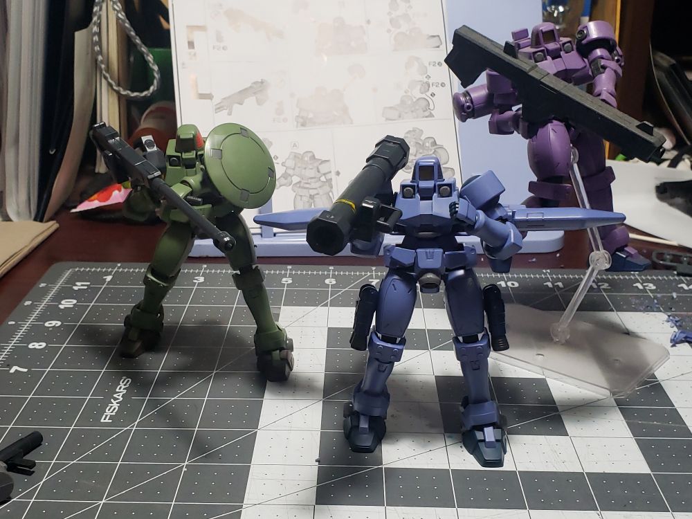 Three plastic model robots in 1/144 scale.  From L to R is a green Leo with a large artillery piece, teal flight unit Leo with a bazooka, and on the stand is a purple Leo "flying" with a beam bazooka.
All not being cannon fodder for the Gundams, for now.