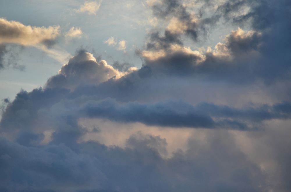image of clouds with different bands of colour and light, and a glow of the sun back lighting clouds at the top