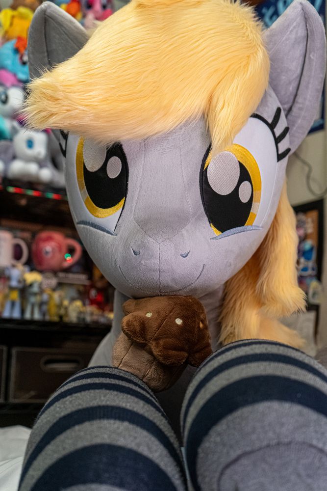 Lifesize Derpy plushie focused on her adorable expression and a plush muffin held between her forelegs and mouth.
