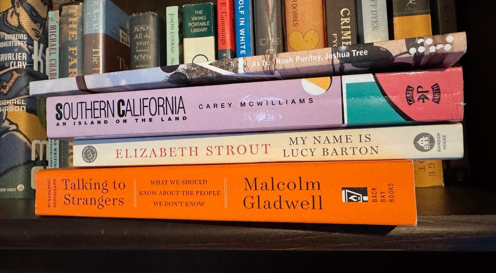 Stack of four books, spines out, at edge of bookshelf