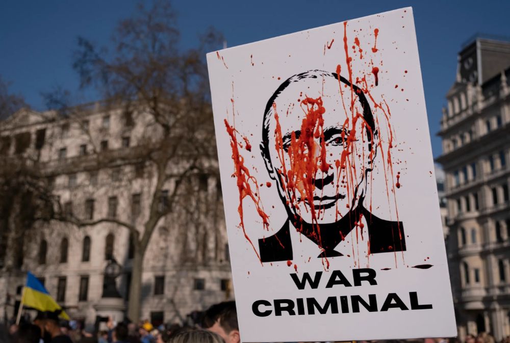 Kuvassa mielenosoittajan plakaatti, jossa putinin kasvokuva veriroiskeilla ja ”War criminal” -tekstillä.