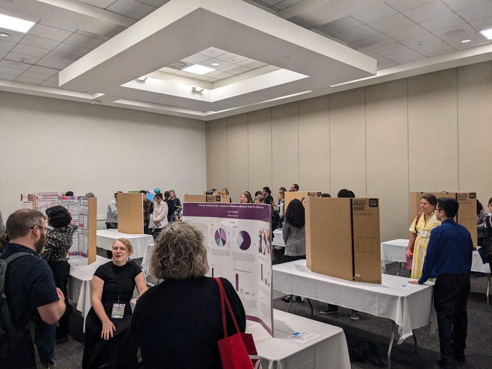 Various people standing in front of poster boards, talking to other people who are listening.
