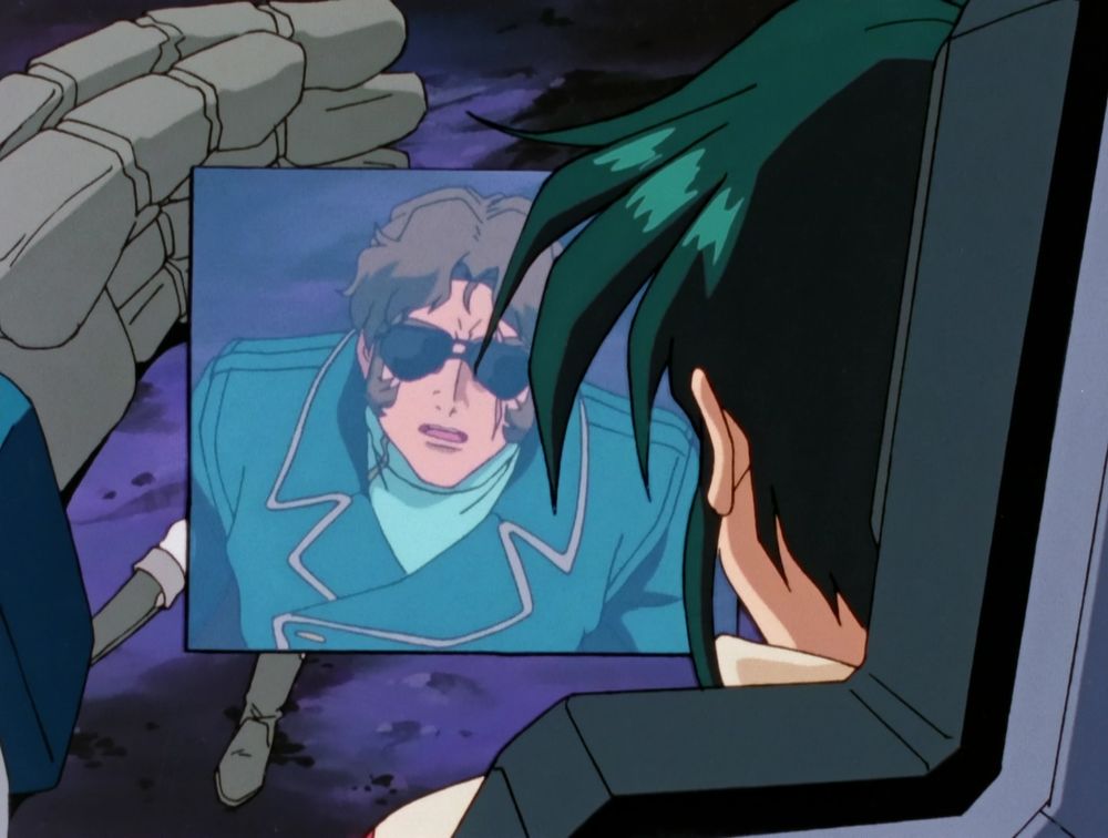 screenshot of jamil sprawled out on the ground and being shielded by the gundam x's hand while garrod's viewscreen shows a zoomed in image of jamil speaking