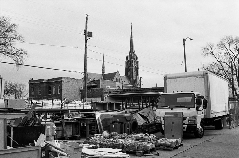 A series of packages delivered outside of building with a large white truck in the foreground and a catholic church in the background. 