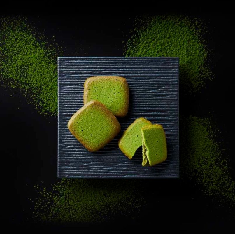 モロゾフの茶久利の商品写真。黒いざらざらした皿の上に、宇治抹茶を練り込んだクッキー「茶久利」が3つ並べられている。2つは重なり合うように置かれ、1つは半分に割って商品断面が見えるようになっている。2枚のクッキーの間にクリームが挟まっている。