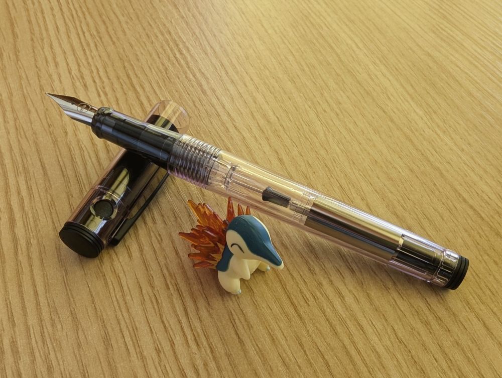 Pilot の万年筆 Lightive の写真。キャップを開けてキャップに軸を載せるように机に置いてある。横にヒノアラシの小さなフィギュアが添えてある。