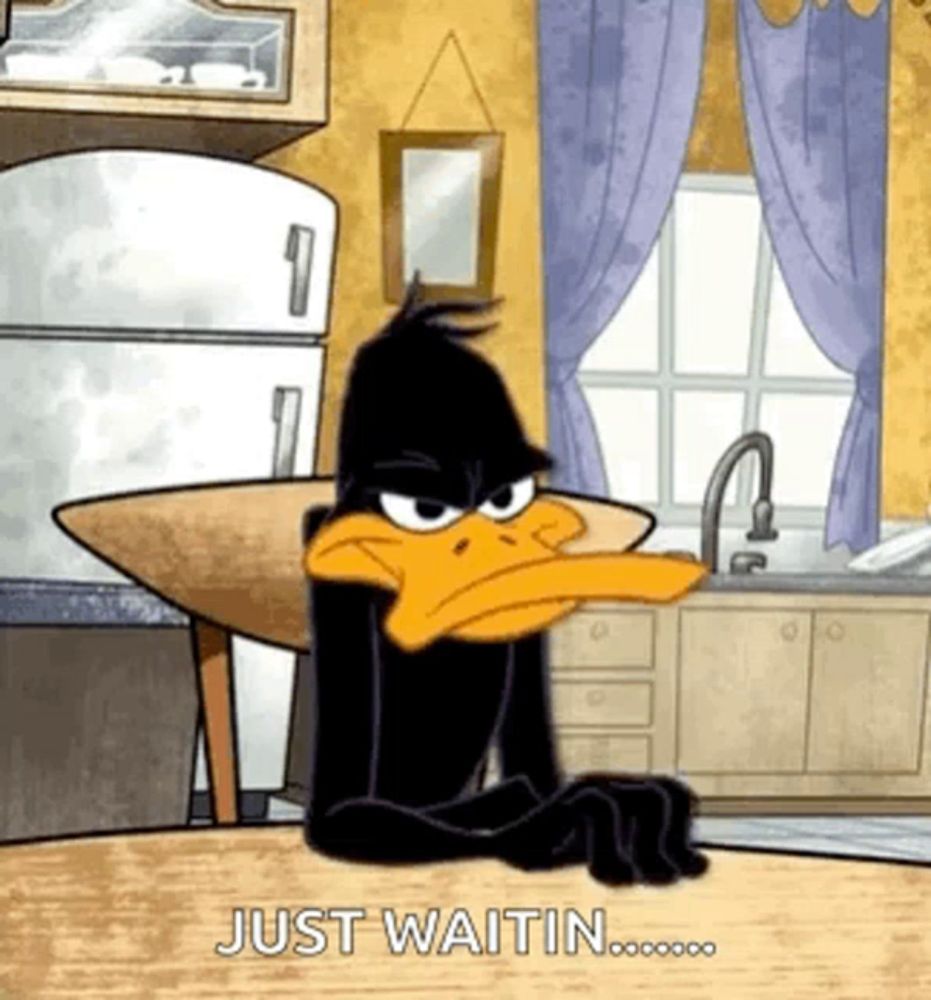 daffy duck is sitting at a table in a kitchen waiting for something .