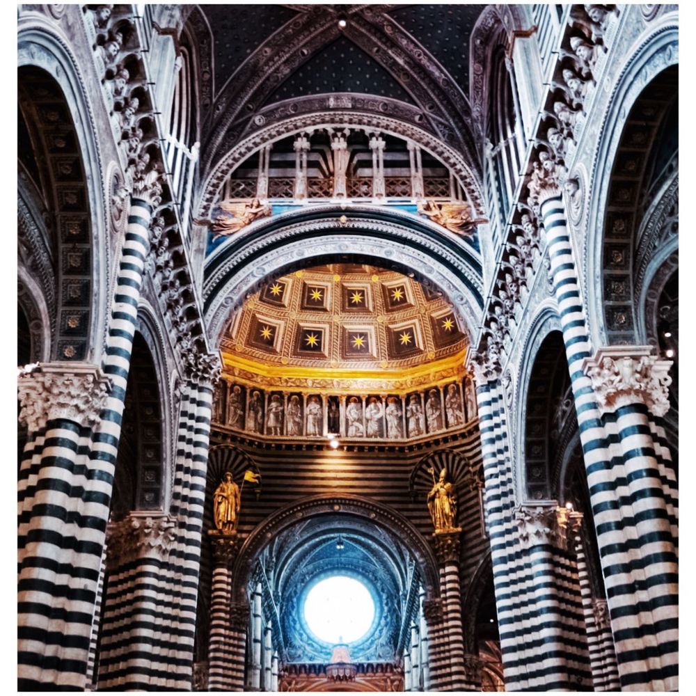 Interior of the Siena Duomo in Italy, zoomed in on part of the dome, supported by ornate columns constructed by black and white marble in stripes. 