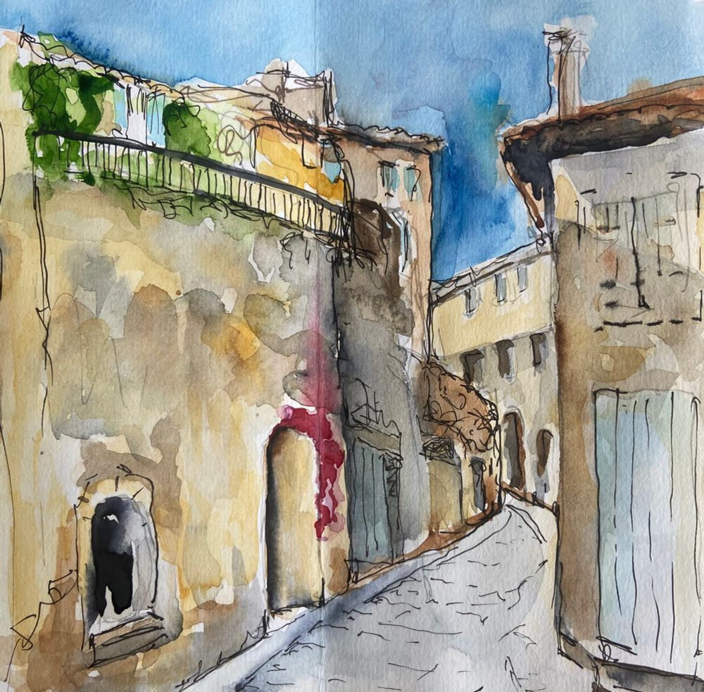 A pen and wash watercolour study of a street in Provence. The narrow street disappears around a corner. The house walls are a pale yellow sandstone