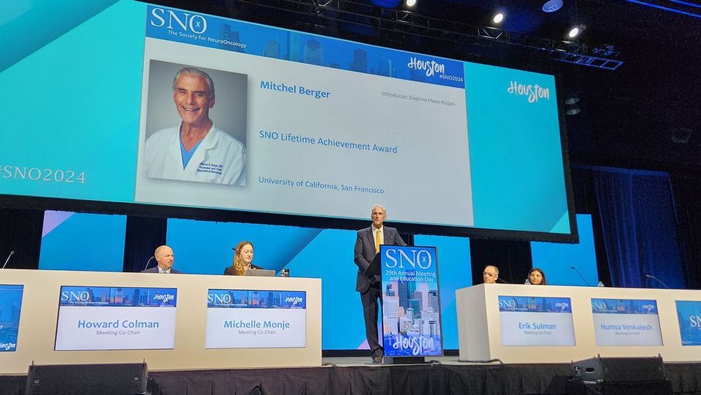UCSF Brain Tumor Center director Mitchel Berger, MD, stands on stage and delivers his acceptance speech for the Lifetime Achievement Award from SNO. Meeting co-chairs Howard Coleman, MD, PhD, Michelle Monje, MD, PhD, Erik Sulman, MD, PhD, and Humsa Venkatesh, PhD, are seated on either side of him.