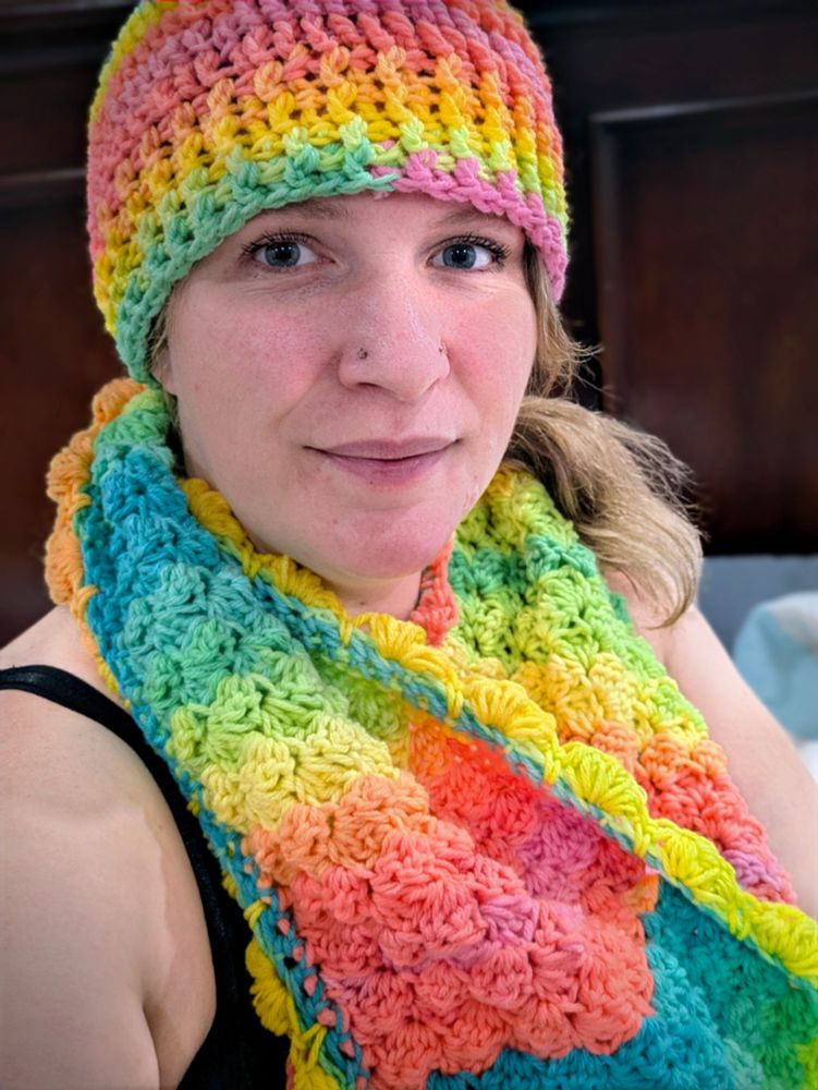 Kallie, white woman who is extra pale from not feeling well, looking pleased while wearing crochet scarf and toque. The toque fits perfectly.