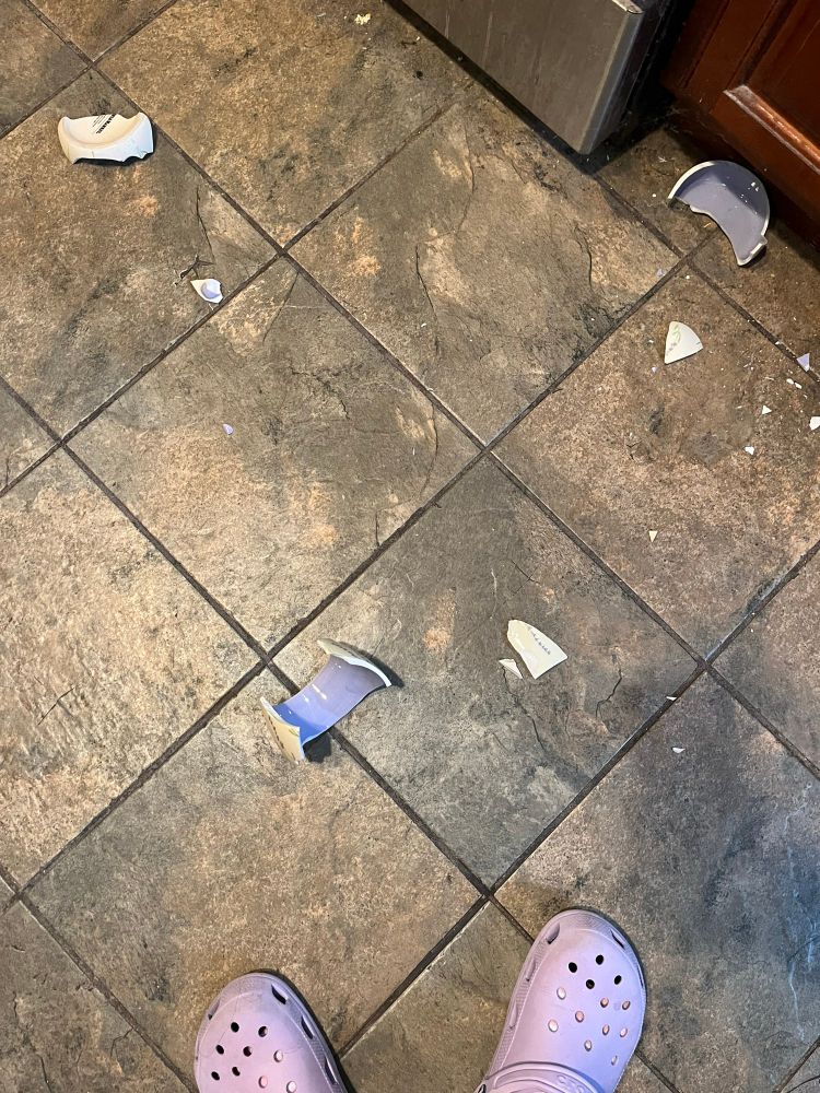 shattered pieces of a mug on a tile floor with my crocs in frame