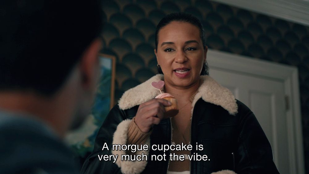 Kaya holding a heart cupcake looking a bit grossed out saying "a morgue cupcake is very much not the vibe" on Elsbeth