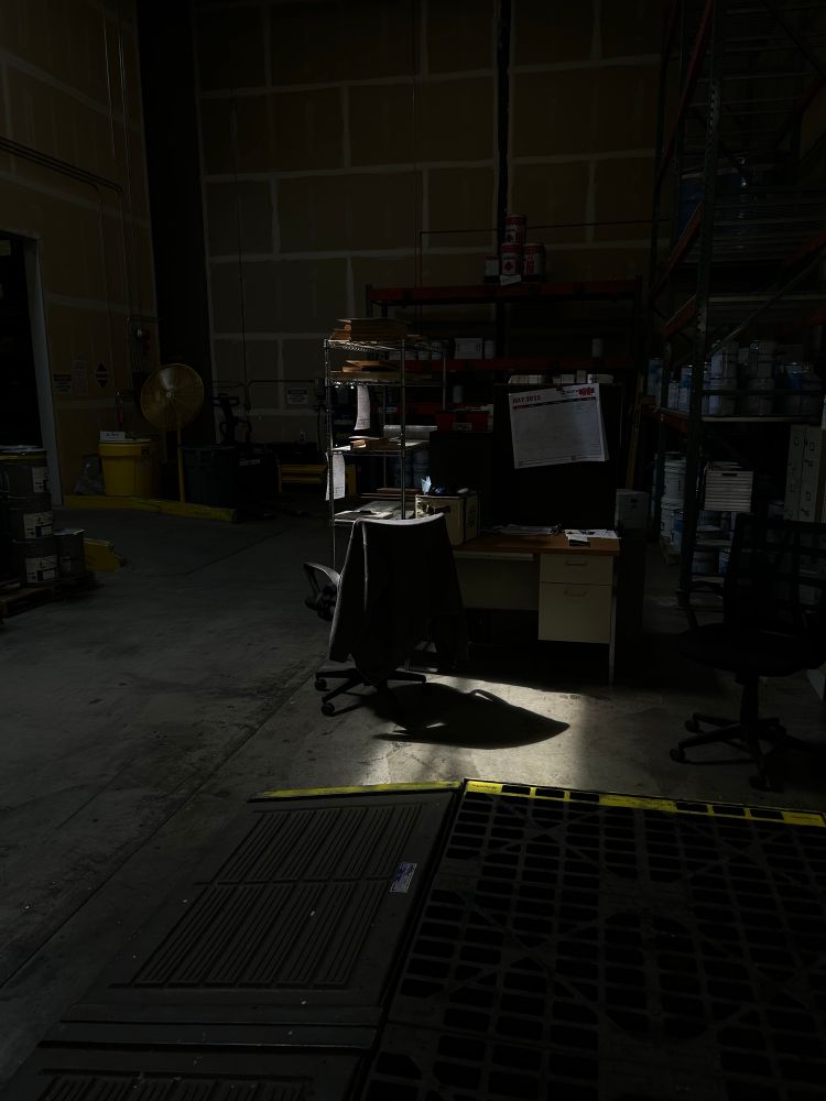 Photo. A dark warehouse, skylight highlighting a desk chair.