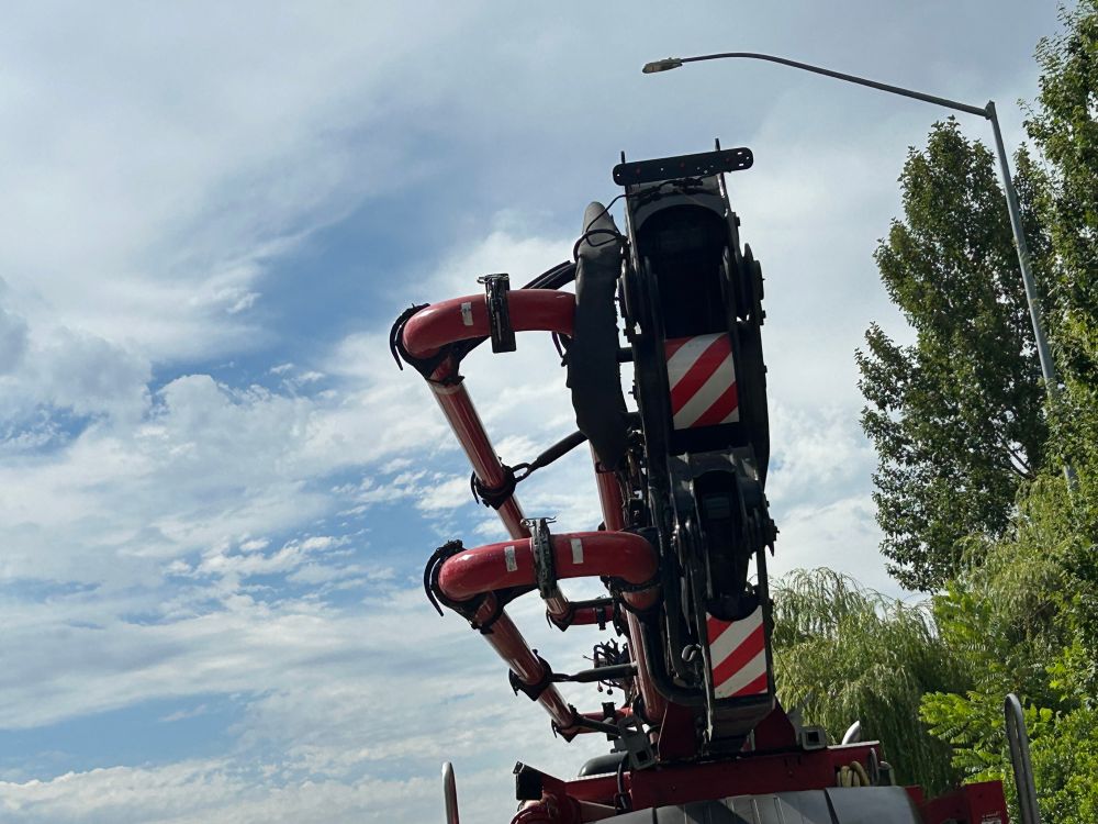Photo. A concrete pumping truck, seen from a bit below, against a partially cloudy sky.
