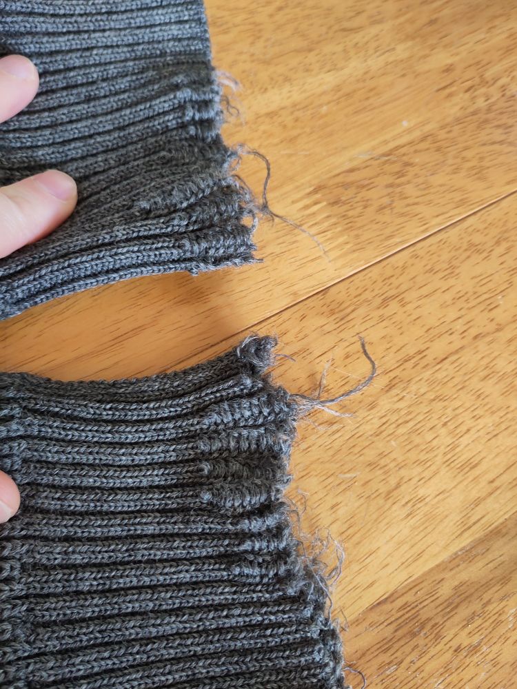 Ragged unravelled ends of a grey wollen jumper 