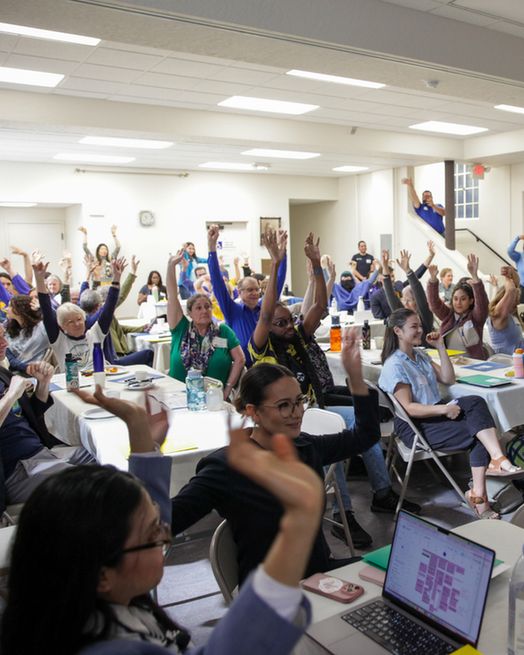 A room full of people holding up their hands.