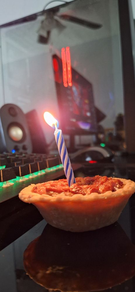 A tiny pecan pie with a little candle in it, a gaming pc in the background 