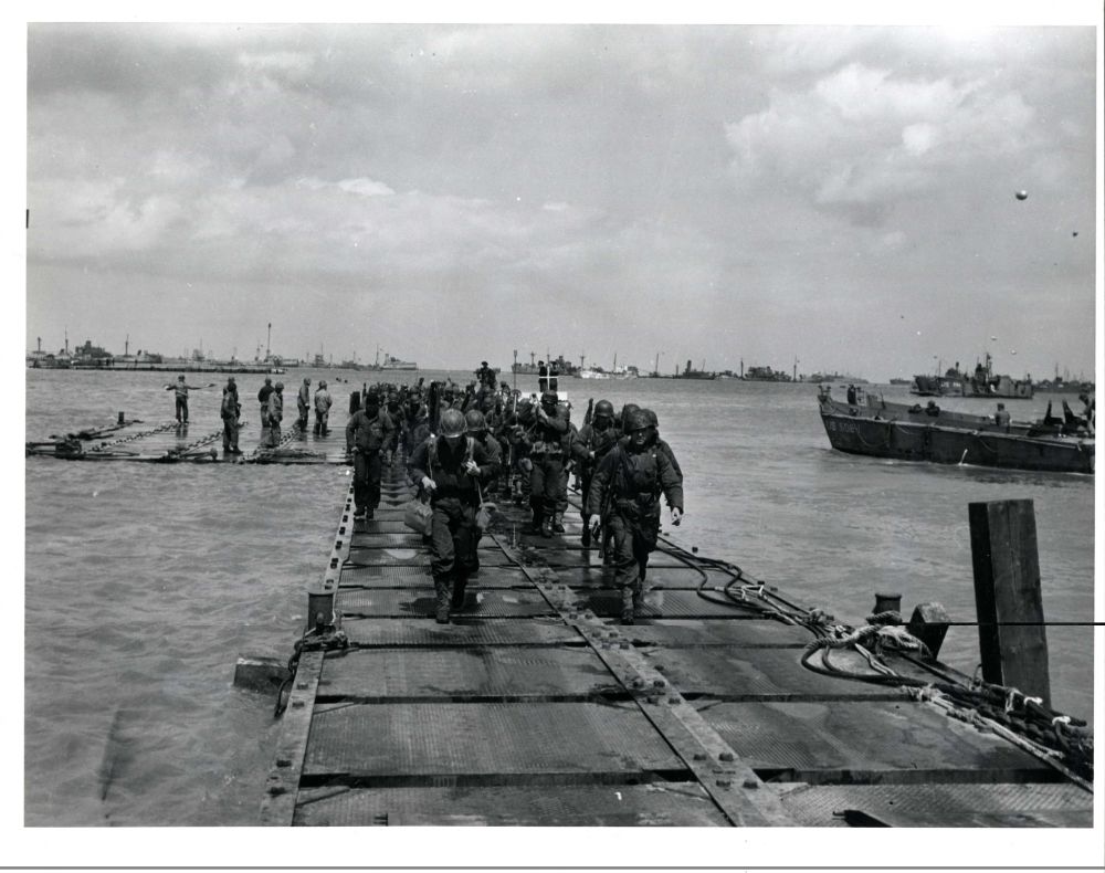 Photo Courtesy of the National Archives.

Original caption: Soldiers coming ashore on a pontoon causeway built by the SeaBees. This causeway was laid down at Omaha Beach during the Normandy Invasion.

NAID: 6682629