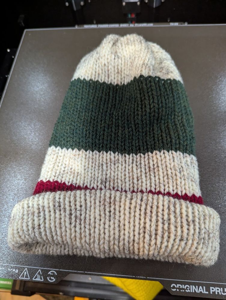 knit beanie hat, with 20 rows of "wheat" at the top, followed by 20 rows of "forest green heather", followed by a stripe of 10 rows of wheat, then 20 rows of "cranberry", except that the brim of the hat covers up most of the cranberry stripe.