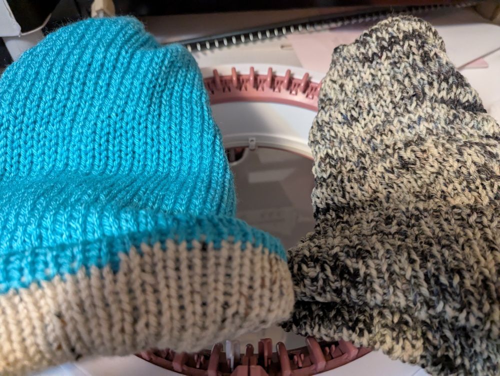 Blue body hat with heather gray brim on the left, with black and white speckled hat on the right, resting on Sentro 48 circular knitting machine