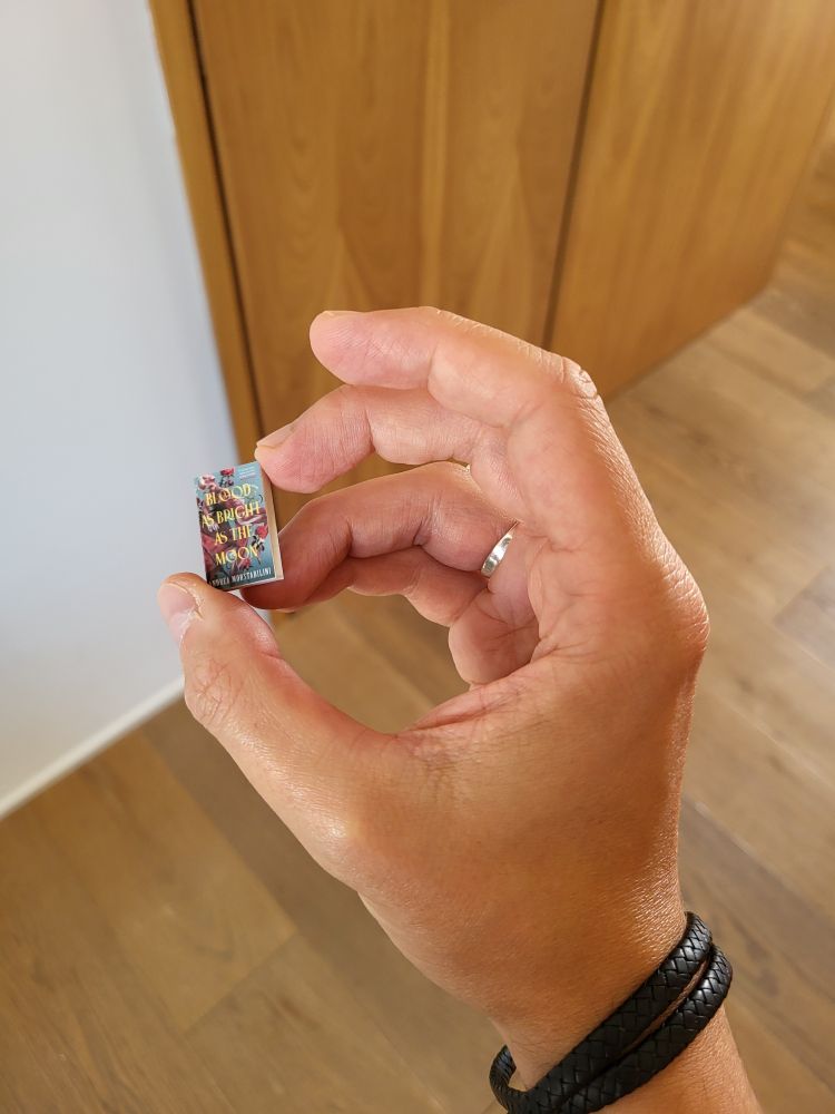 The pin, held by a hand, for size reference. 
