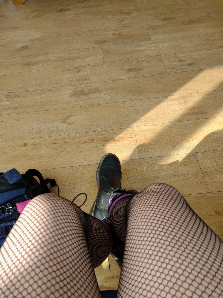 Holzdielen Wartezimmerboden.
Am unteren Bildende die Beine der wartenden Person gehüllt in Netzstrumpfhose und Doc Martens