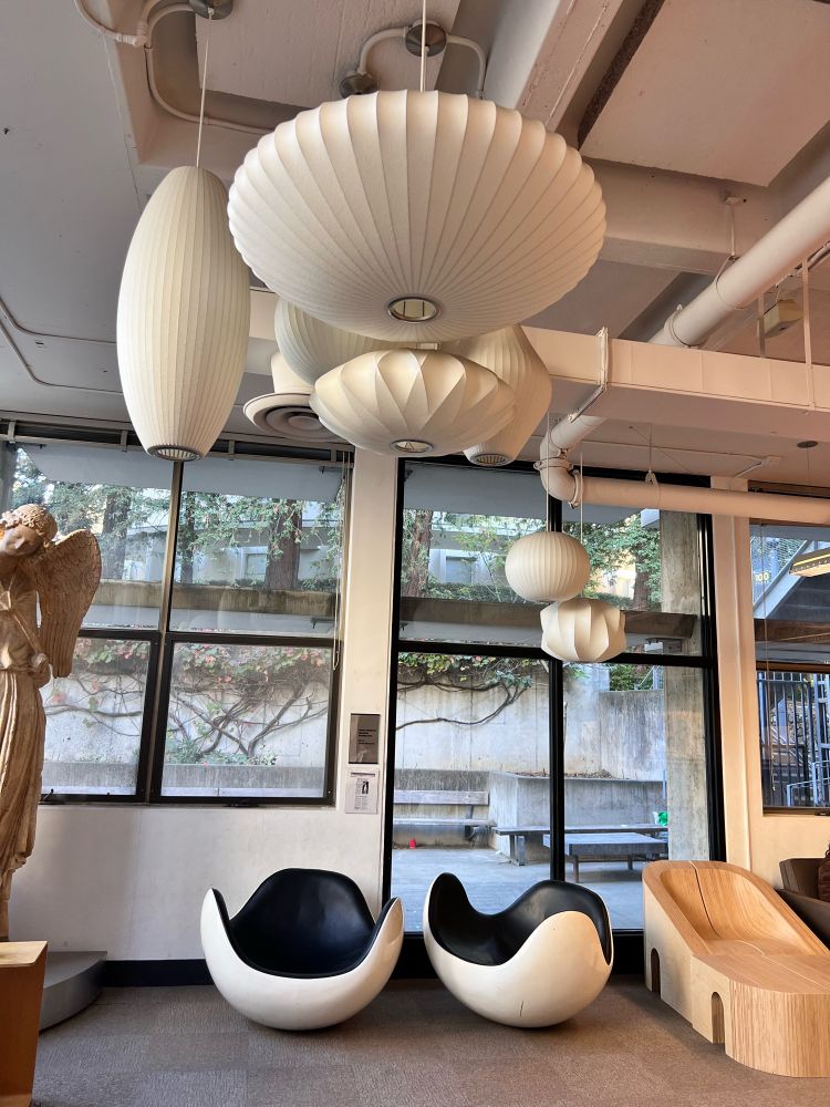 Several Herman Miller saucer lamps, two space age mod chairs, inside of a library. 