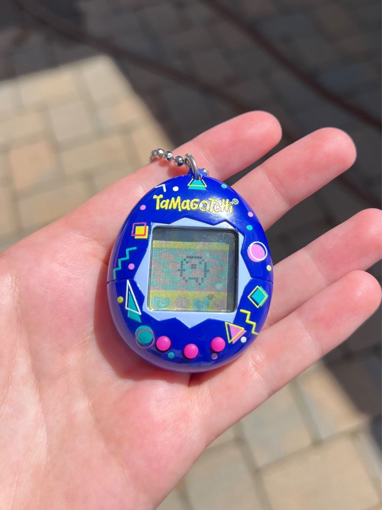 Blue tamagotchi toy with a 3rd stage tamagotchi pet - he’s got little arms and legs now and he’s dancing in the screen