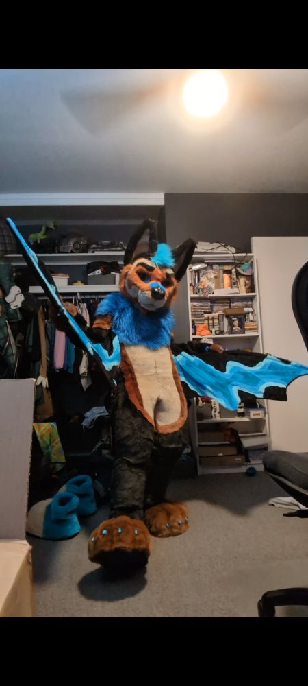 A fursuit of a brown and black flying fox. The wings have blue sound wave patterns in them. 