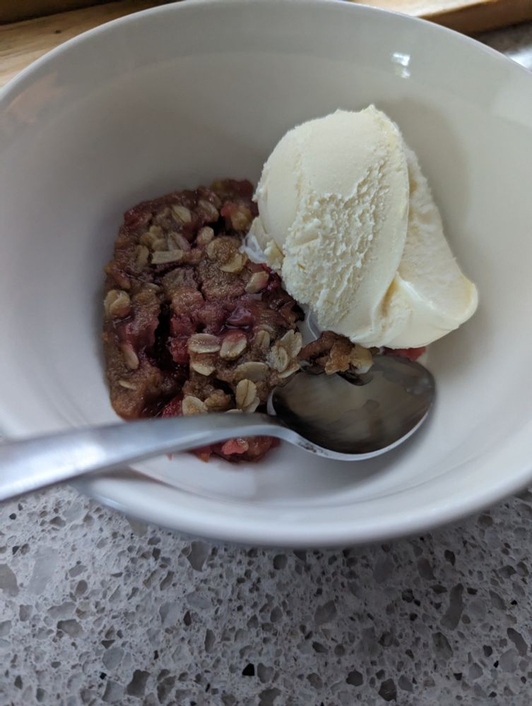 Bourbon cherry crisp dessert in a bowl with a scoop of vanilla ice cream. Spoon crossing the foreground as this serving is ready to go 