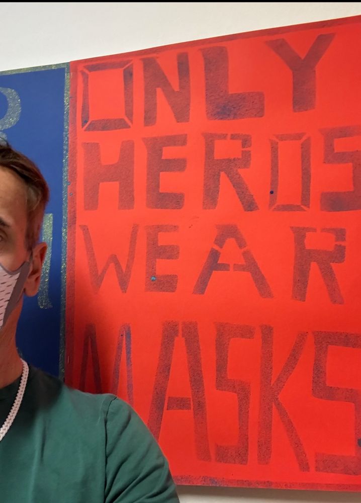Ausschnitt einer Person mit FFP3-Maske vor einem roten Kunstwerk mit der Aufschrift ins dunkelrot: Only Heros wear masks.
