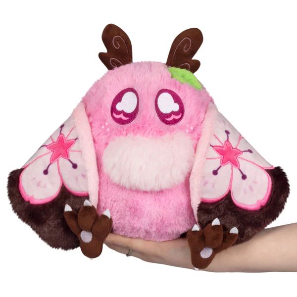 a light Pink mothman plushie with sakura flowers on the wing design with a small green leaf on its head