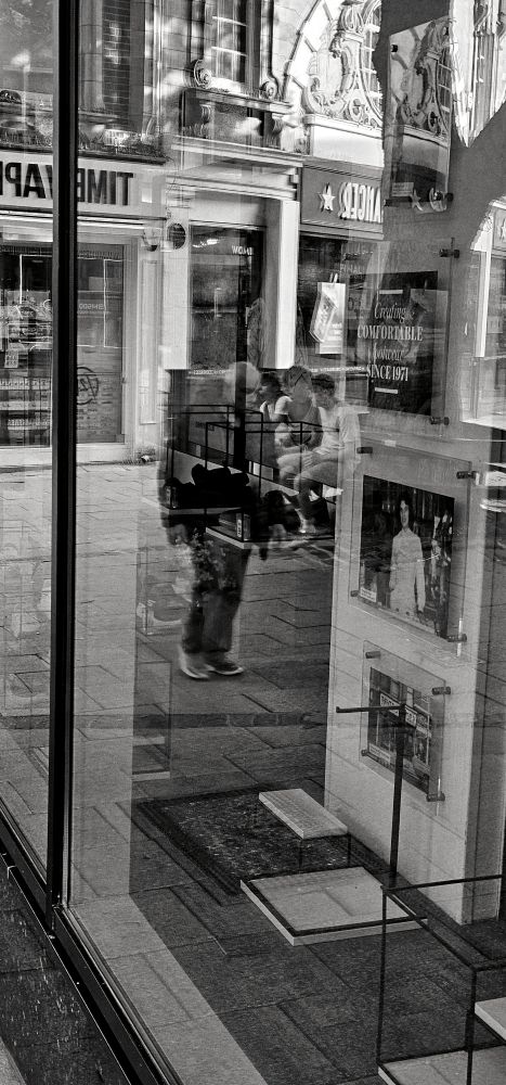 A black and white photo of the reflections of people on a street.