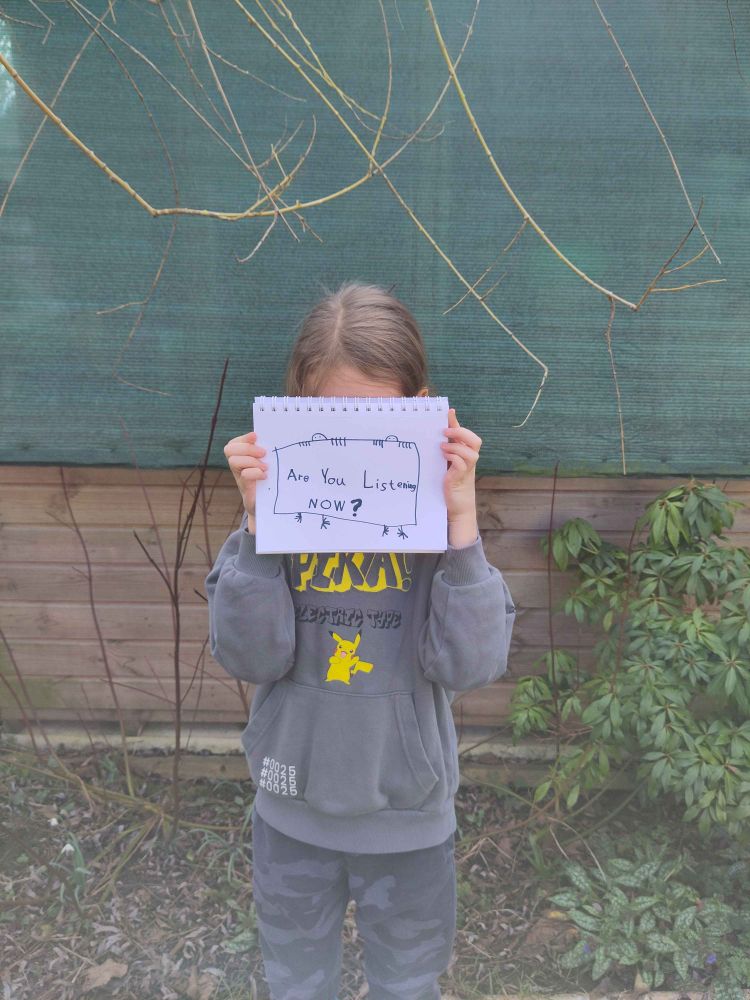 A child holding a sign that reads "Are you listening NOW?"